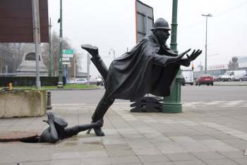 una composizione di sculture a Bruxelles, 2012, da un tombino emerge una mano che fa inciampare un poliziotto.