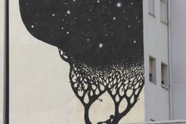 foto di un Murale sulla parete di una casa di un quartiere popolare di Madrid. Al di là dell'inferriata un uomo sdraiato su un ramo guarda i rami dell'albero pieni di stelle